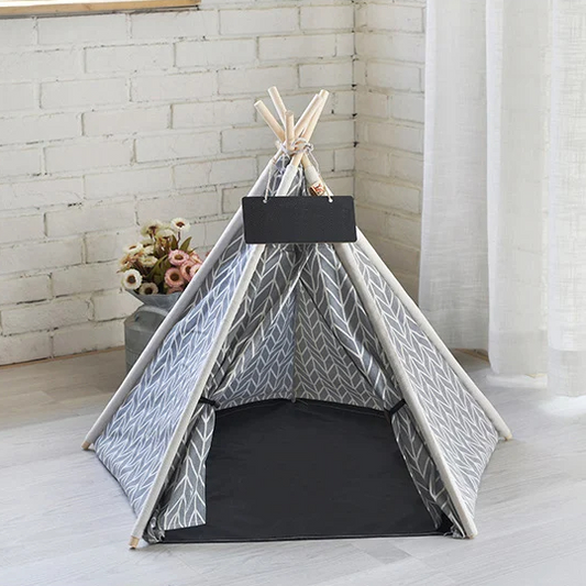 Maison pour Chat Pliable de Style Tipi Indien posée au sol sur un parquet sur fond d'un mur en briques blanc avec un pot de fleur au sol